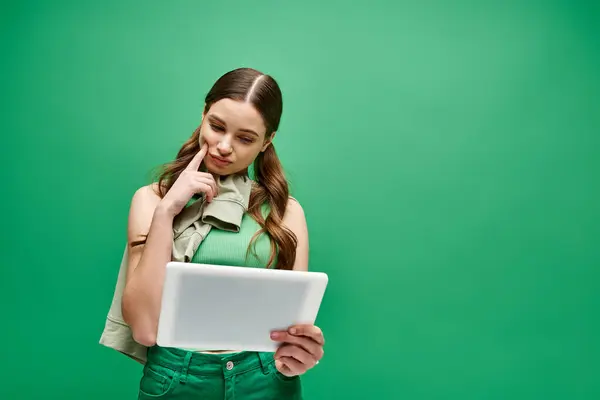 Mujer joven con camisa verde muestra tableta blanca en el entorno del estudio. - foto de stock