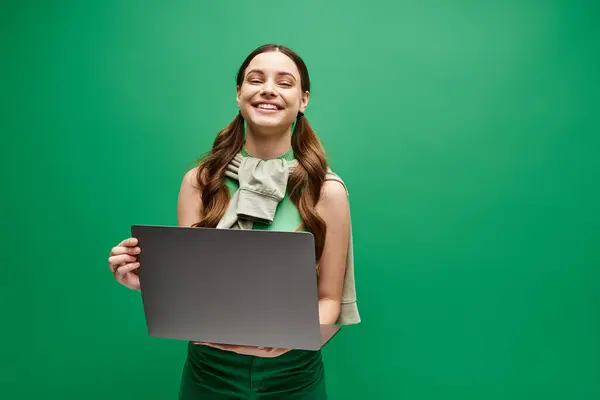 Жінка в 20 років тримає ноутбук перед яскраво-зеленим тлом, виключаючи цифрові розширення та з'єднання. — стокове фото