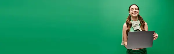 A young woman in her 20s holding a laptop in front of a vibrant green background. — Stock Photo