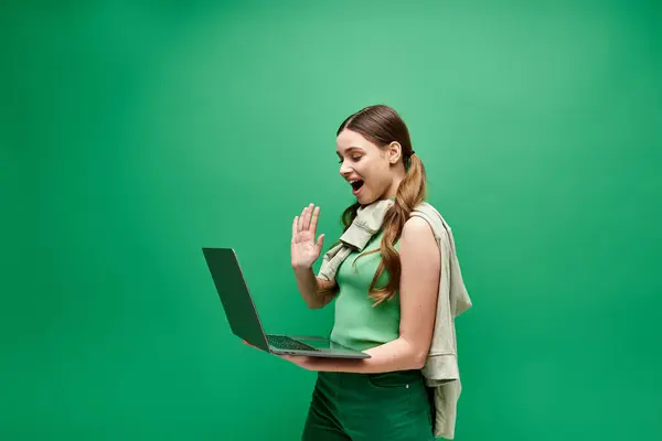 A young woman in her 20s, dressed in a vibrant green gown, holds a laptop in a modern studio setting. — Stock Photo