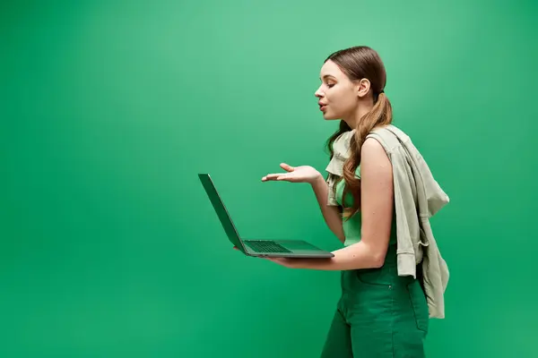 A young woman in her 20s holding a laptop in a studio setting on a green background. — Stock Photo