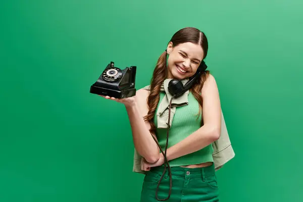 A young woman in her 20s holds a phone, smiling happily in a studio setting with a green background. — Stock Photo