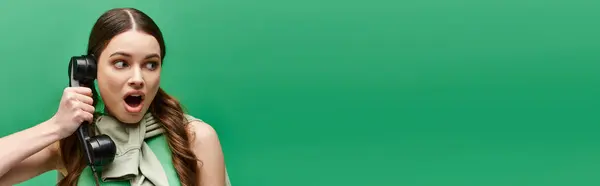 Une jeune femme dans la vingtaine tient un téléphone sur son visage, perdue dans la conversation ou la contemplation dans un studio avec un fond vert. — Photo de stock