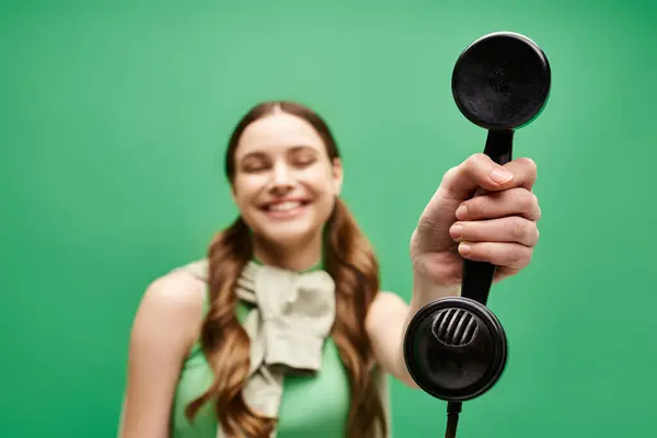 Una joven hermosa mujer de unos 20 años sosteniendo un teléfono vintage sobre un fondo verde vivo. - foto de stock