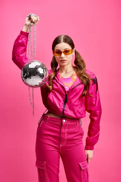 Giovane donna sulla ventina, elegante in rosa, tiene una palla da discoteca in un vivace studio con uno sfondo rosa. — Foto stock