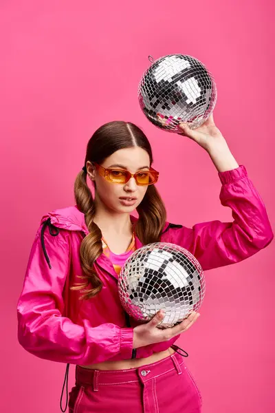 Uma jovem elegante de 20 anos segurando duas bolas de discoteca contra um fundo rosa, exalando uma vibração glamourosa e divertida. — Fotografia de Stock
