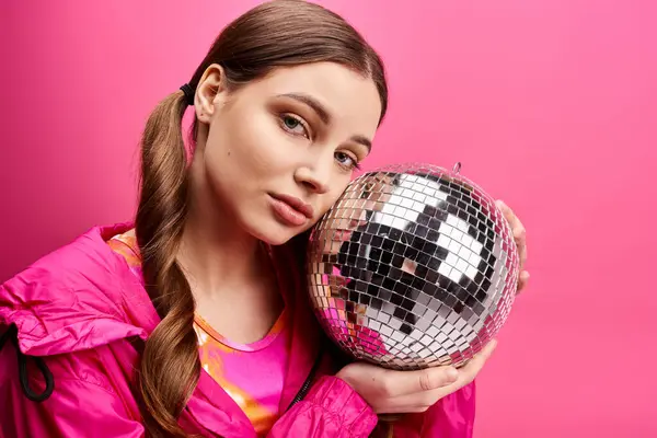 A young woman in her 20s holds a disco ball in front of her face, radiating a sparkling and glamorous aura against a pink background. — Stock Photo