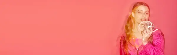 A young woman in a pink dress elegantly holds a disco ball, creating a dreamy and magical atmosphere in a studio with a pink background. — Stock Photo