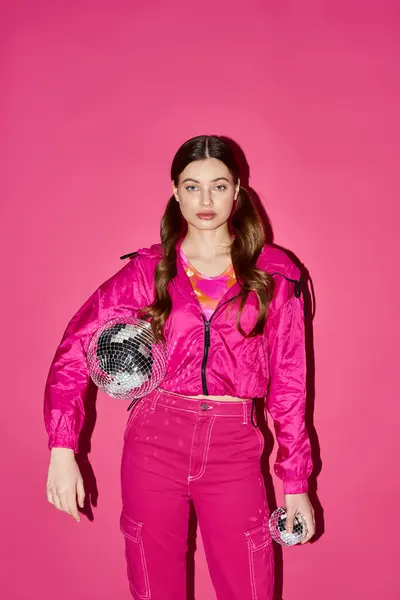 Une femme à la mode dans la vingtaine, vêtue d'une tenue rose, prend une pose confiante dans un cadre de studio avec un fond rose. — Photo de stock