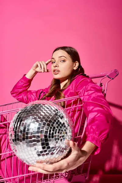 Una giovane donna elegante sulla ventina, vestita di rosa, che tiene una palla da discoteca in uno studio accattivante. — Foto stock