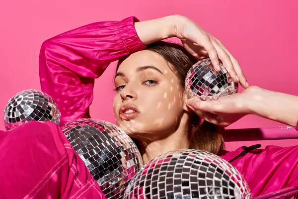 Une jeune femme élégante dans la vingtaine portant une tenue rose, tenant des boules de disco dans un cadre studio vibrant avec fond rose. — Photo de stock