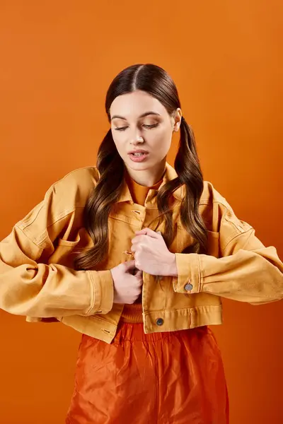 A beautiful young woman in her 20s dressed in an orange shirt and pants against backdrop in a studio setting. — Stock Photo