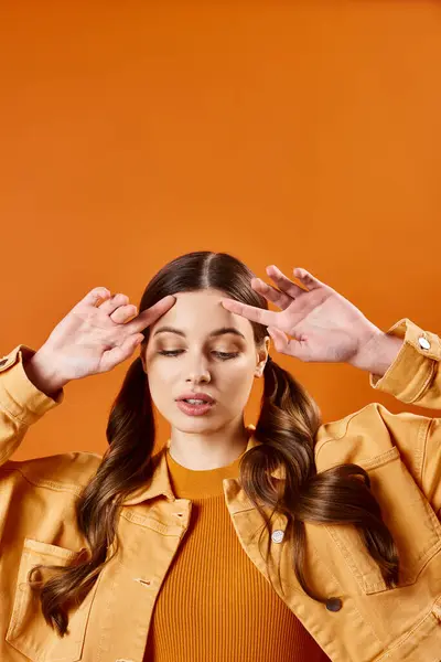 A young woman in her 20s with her hands on her head in a studio setting with an orange background, looking overwhelmed. — Stock Photo