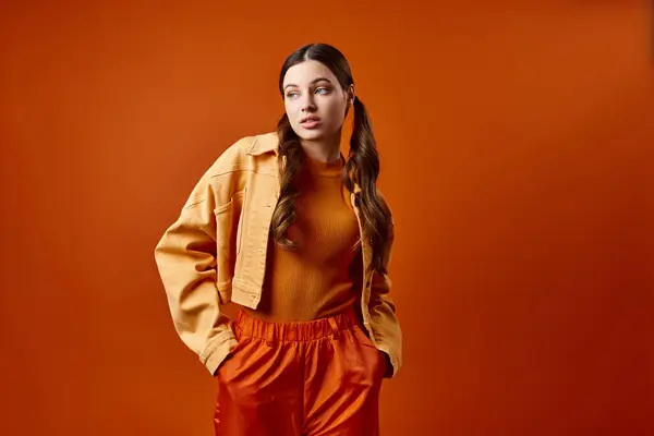 Eine stilvolle Frau in ihren Zwanzigern steht selbstbewusst vor leuchtend orangefarbener Kulisse in einem Studio-Setting. — Stockfoto