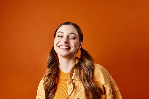 A stylish young woman in her 20s with long hair wearing a bright yellow shirt, posing in a studio setting with an orange background. — Stock Photo