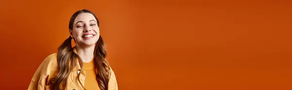 Uma jovem, bela mulher na casa dos 20 anos está confiante na frente de uma parede laranja vibrante em um estúdio. — Fotografia de Stock