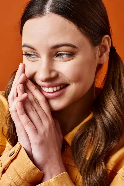 Молодая стильная 20-летняя женщина, ярко улыбающаяся руками на фоне оранжевой студии. — стоковое фото