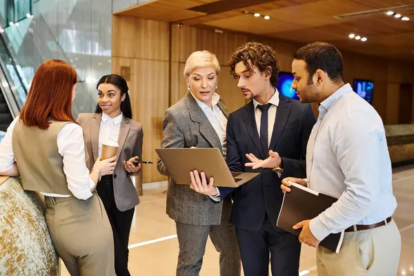 Diverse group of business professionals gathered around a laptop, discussing and collaborating. — Stock Photo