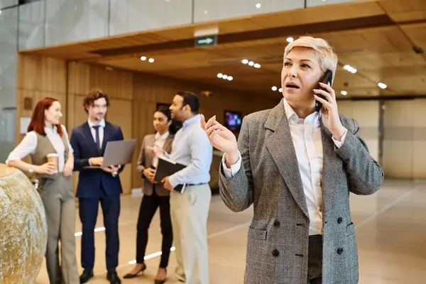 A woman speaking on a cell phone in front of a diverse group of business people. — Stock Photo