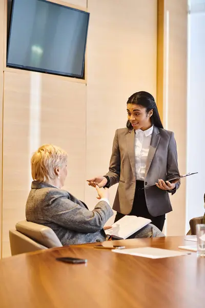 A woman confidently presents to another woman in a conference room. — Stock Photo