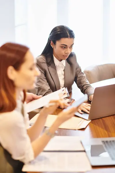 Two women of different ethnicities work intently on a laptop at a table. — Stock Photo