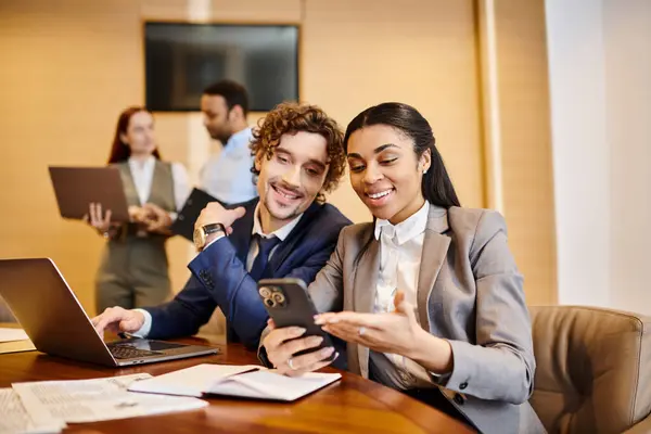 An interracial man and woman engrossed in a cell phone at a table. — Stock Photo