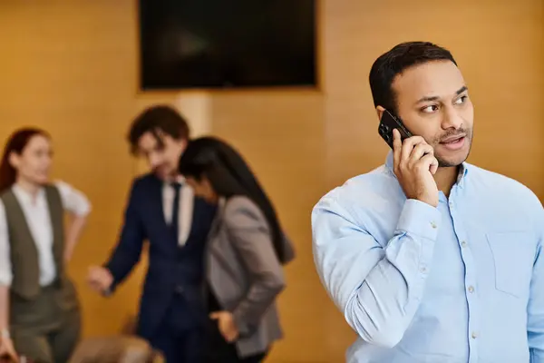 A man stands in front of an interracial group, speaking on a cell phone. — Stock Photo