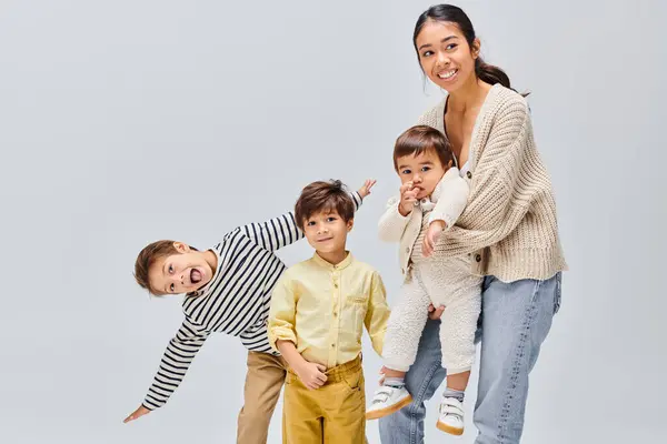 Asian mother gracefully poses with her children in a studio against a grey backdrop, glowing with love and joy. — Stock Photo