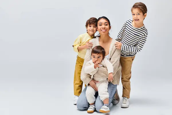 A young Asian mother and her children strike a pose in a studio against a grey background. — Stock Photo