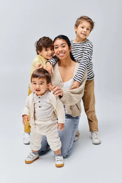 Uma jovem mãe asiática e seus filhos fazem uma pose encantadora em um estúdio contra um fundo cinza. — Fotografia de Stock