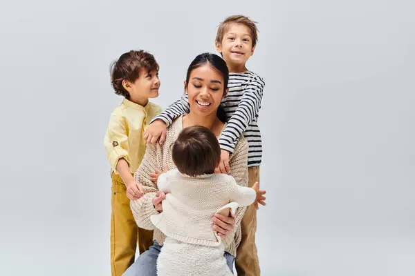A young Asian mother smiles warmly as she lovingly holds her children while looking at the camera in a studio setting. — Stock Photo