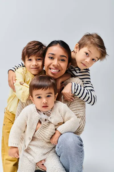 Um grupo de crianças felizes posando juntas em um estúdio para sua jovem mãe asiática em um fundo cinza. — Fotografia de Stock