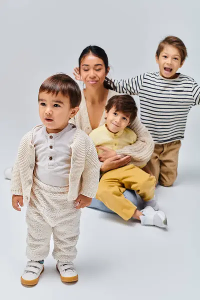 A young Asian mother and her children strike a pose in a studio setting against a grey background. — Stock Photo