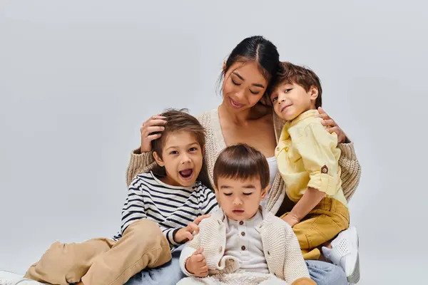 A young Asian mother sits on a bed, surrounded by her children, sharing a moment of peace and love in a studio setting. — Stock Photo
