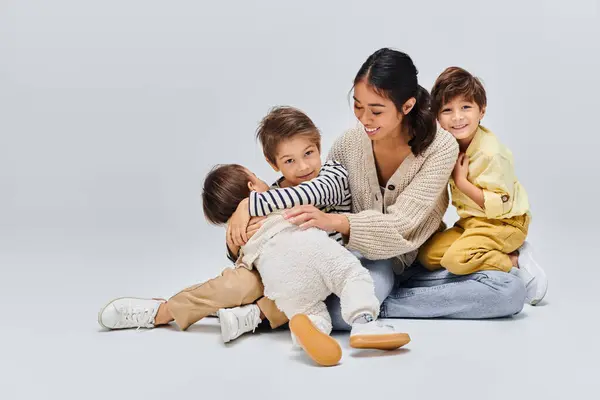 Una giovane madre asiatica seduta a terra circondata dai suoi figli, che condivide un momento di amore e vicinanza. — Foto stock