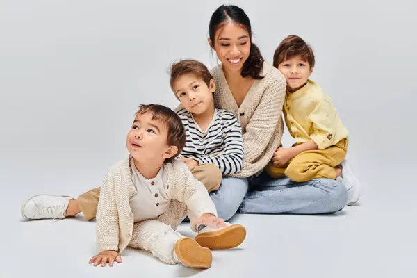 A young Asian mother sits on the ground with children, creating a serene moment of unity and connection. — Stock Photo