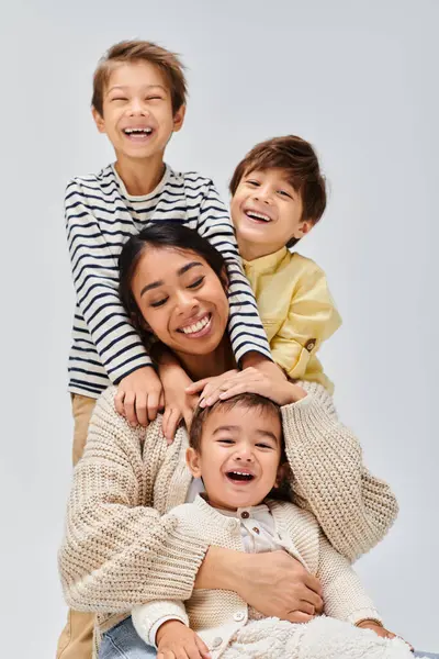 A young Asian mother and her kids playfully stack on top of each other in a studio setting with a grey background. — Stock Photo