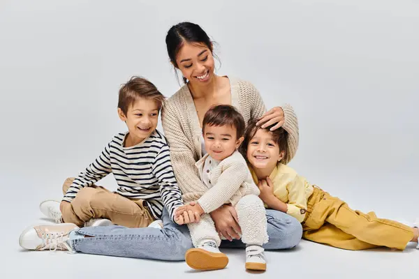 Una joven madre asiática sentada en el suelo con sus hijos, interactuando y creando un vínculo especial en un entorno de estudio. - foto de stock