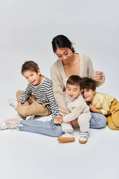 Una joven madre asiática se sienta en el suelo con sus hijos, creando una escena de amor familiar y unión. - foto de stock