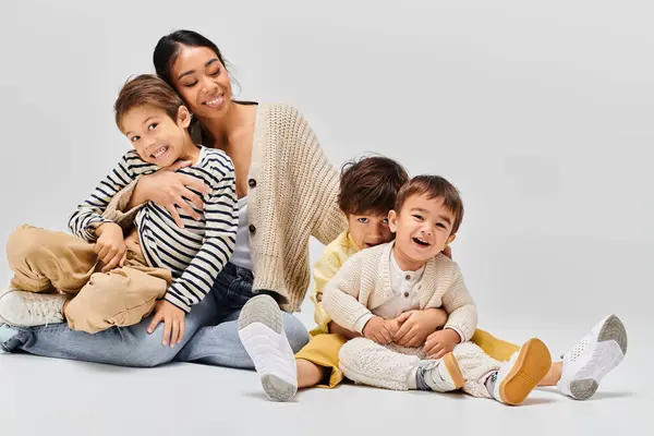 Una joven madre asiática se sienta en el suelo con sus hijos, compartiendo un momento de conexión y amor en un estudio. - foto de stock