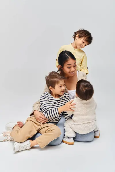 Una joven madre asiática se sienta en el suelo con sus hijos, creando un momento familiar conmovedor en un entorno de estudio. - foto de stock