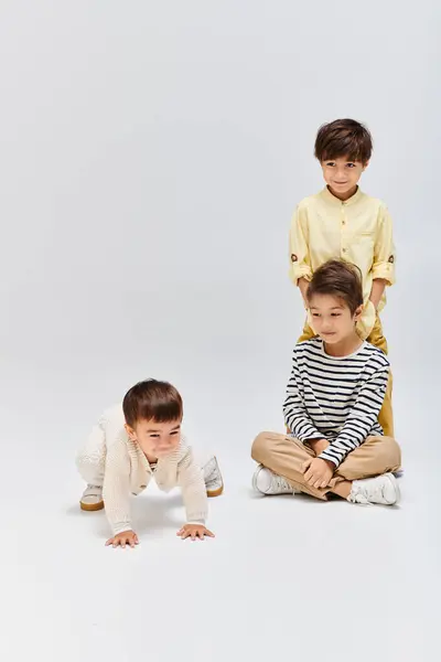 Three young boys are peacefully seated on the ground in front of a white background, exuding a sense of calm. — Stock Photo