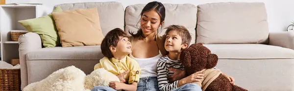 Молода азіатська мати сидить на дивані з двома дітьми в затишній вітальні, займається теплою і люблячою взаємодією. — стокове фото