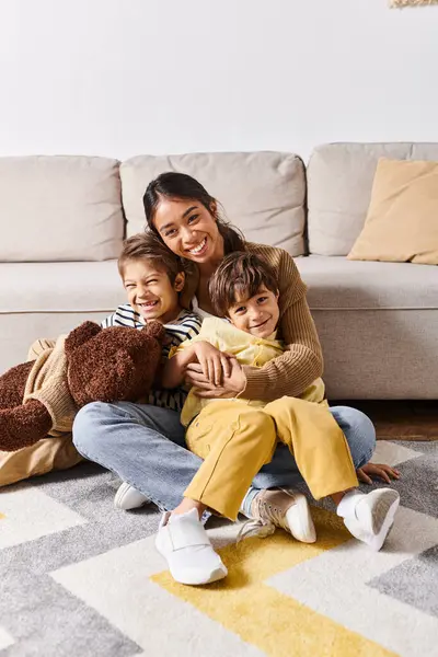 Молода азіатська мати сидить на підлозі з двома маленькими синами в затишній вітальні вдома. — стокове фото