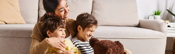 Uma jovem mãe asiática sentada em um sofá com seus dois filhinhos na acolhedora sala de estar. — Stock Photo