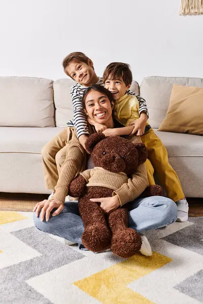 Une jeune mère asiatique assise sur le sol avec ses deux petits fils et un ours en peluche, profitant d'un moment paisible ensemble. — Photo de stock