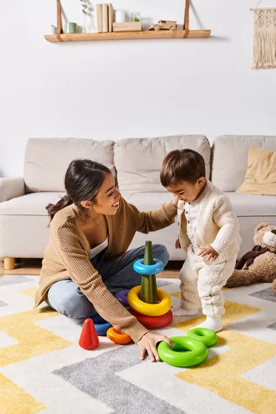 A young Asian mother joyfully interacts with her little son on the floor of their cozy living room. — Stock Photo