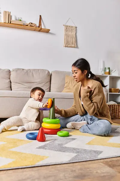 A young Asian mother playing with her little son on the floor of their living room, sharing smiles and laughter. — Stock Photo