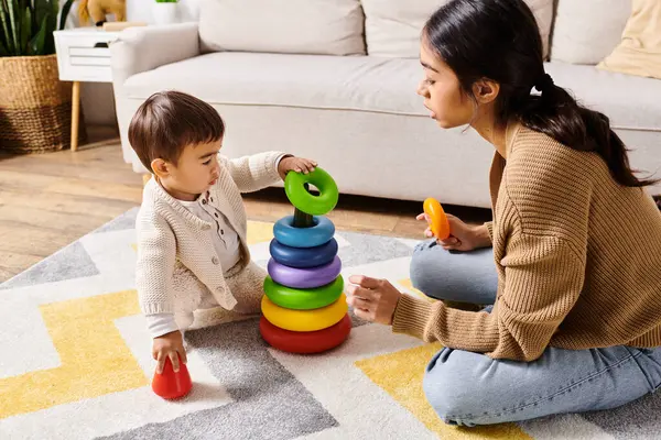 Una giovane madre asiatica interagisce felicemente con il suo piccolo figlio sul pavimento del loro accogliente soggiorno, creando divertenti ricordi insieme.. — Foto stock