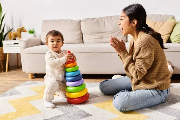 Una giovane madre asiatica si impegna gioiosamente con il suo piccolo figlio sul pavimento del loro accogliente soggiorno. — Foto stock